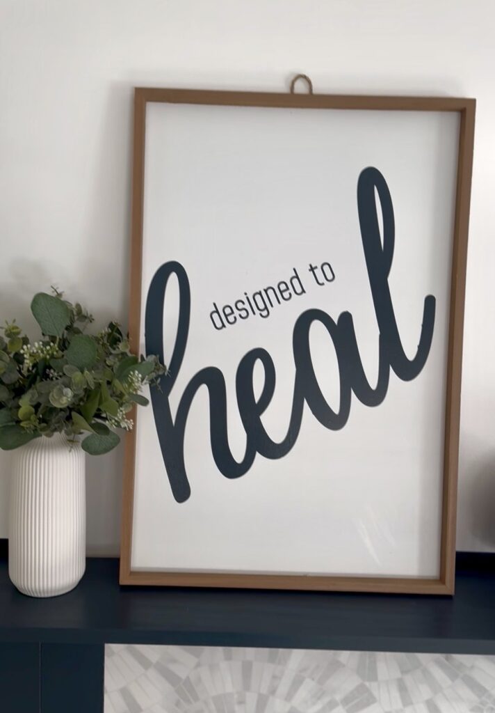 office decor of photo that states "designed to heal" with plant next to photo