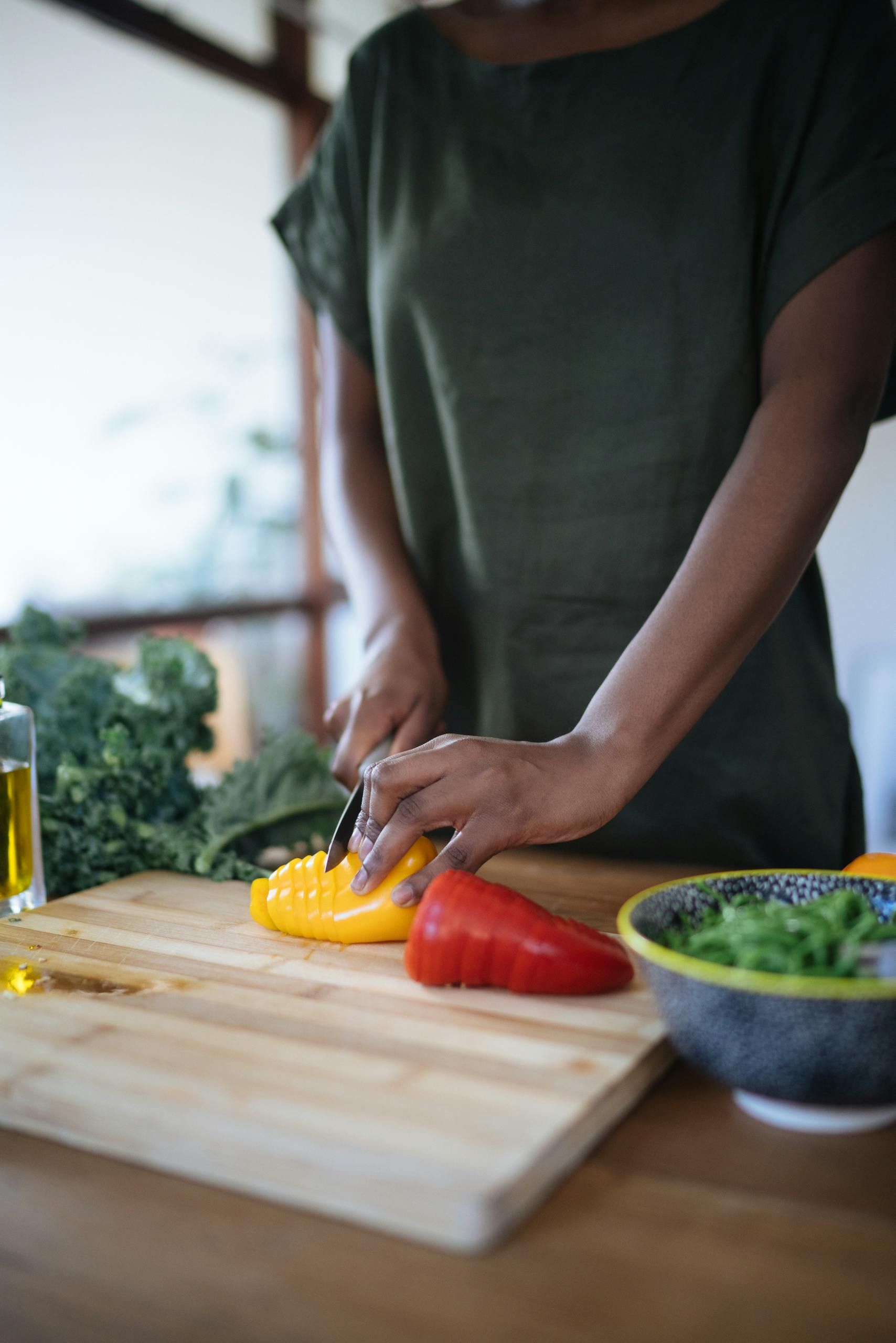 A person slicing colorful bell peppers on a wooden board in a bright kitchen setting.
